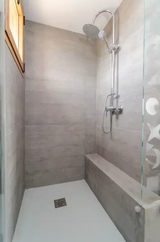 Una zona de ducha revestida de azulejos con ducha de mano y banco integrado.