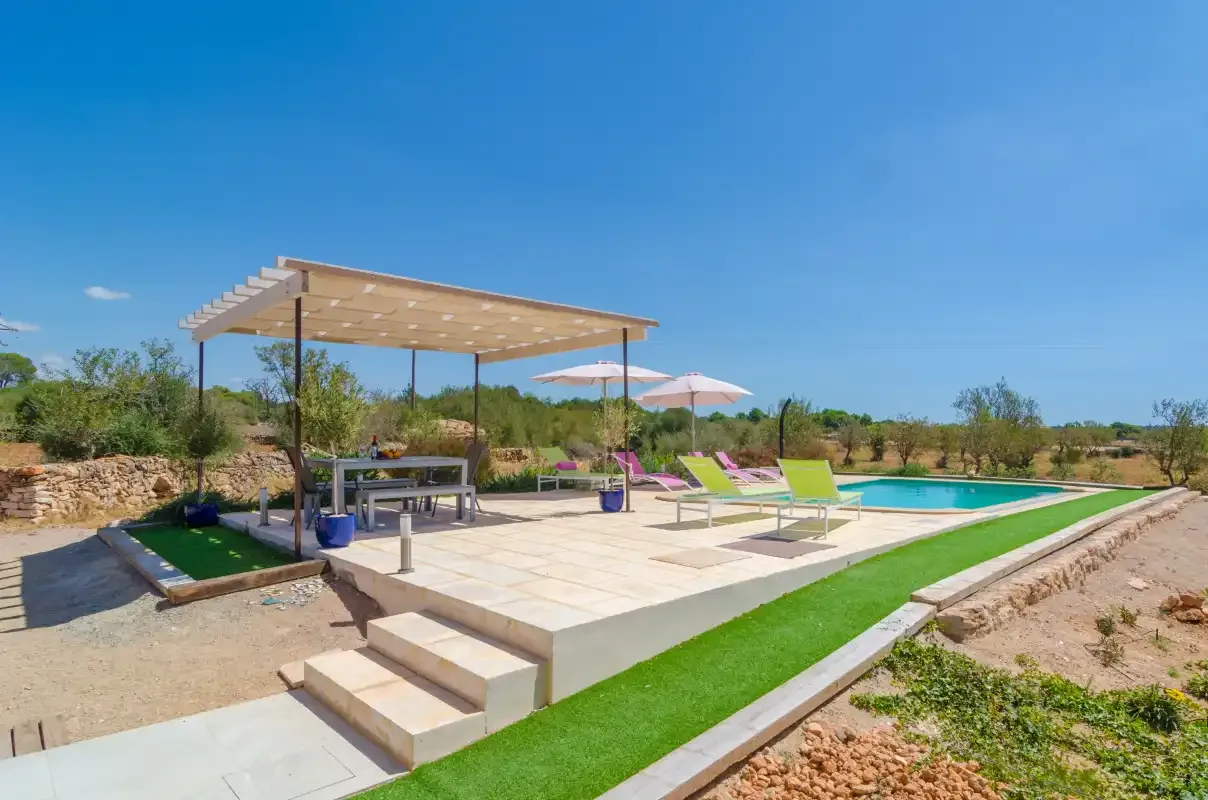 Una piscina exterior junto a un patio pavimentado con pérgola y asientos.