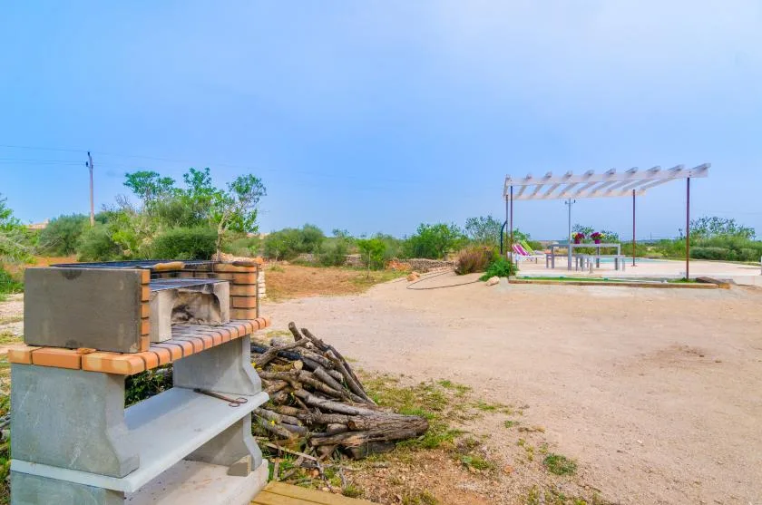Un patio al aire libre cuenta con una barbacoa de ladrillo y una zona de descanso bajo una pérgola.