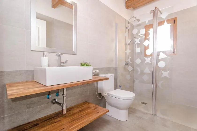 Un baño luminoso con lavabo, inodoro y mampara de ducha de vidrio estampado.
