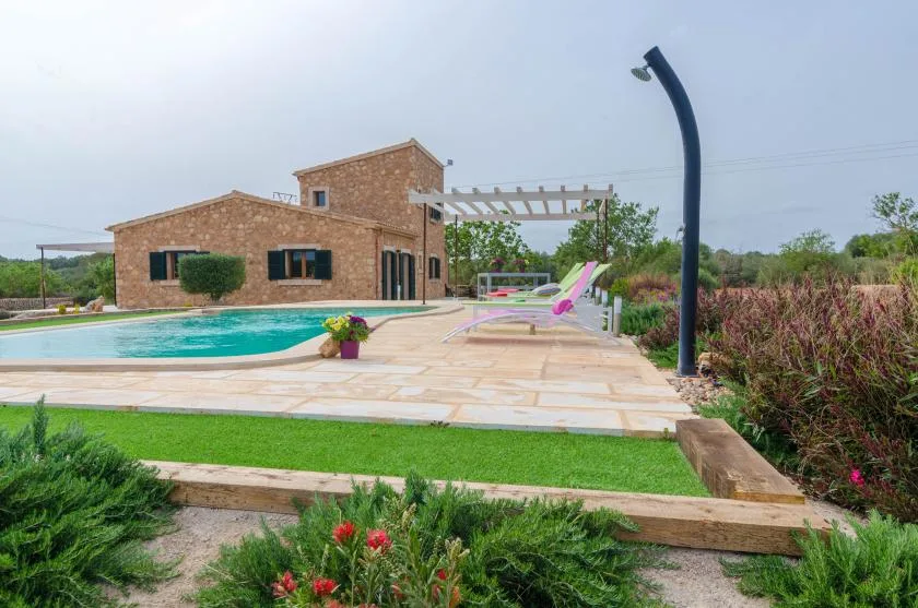 Piscina exterior junto a una casa de ladrillo, con patio pavimentado y jardín.