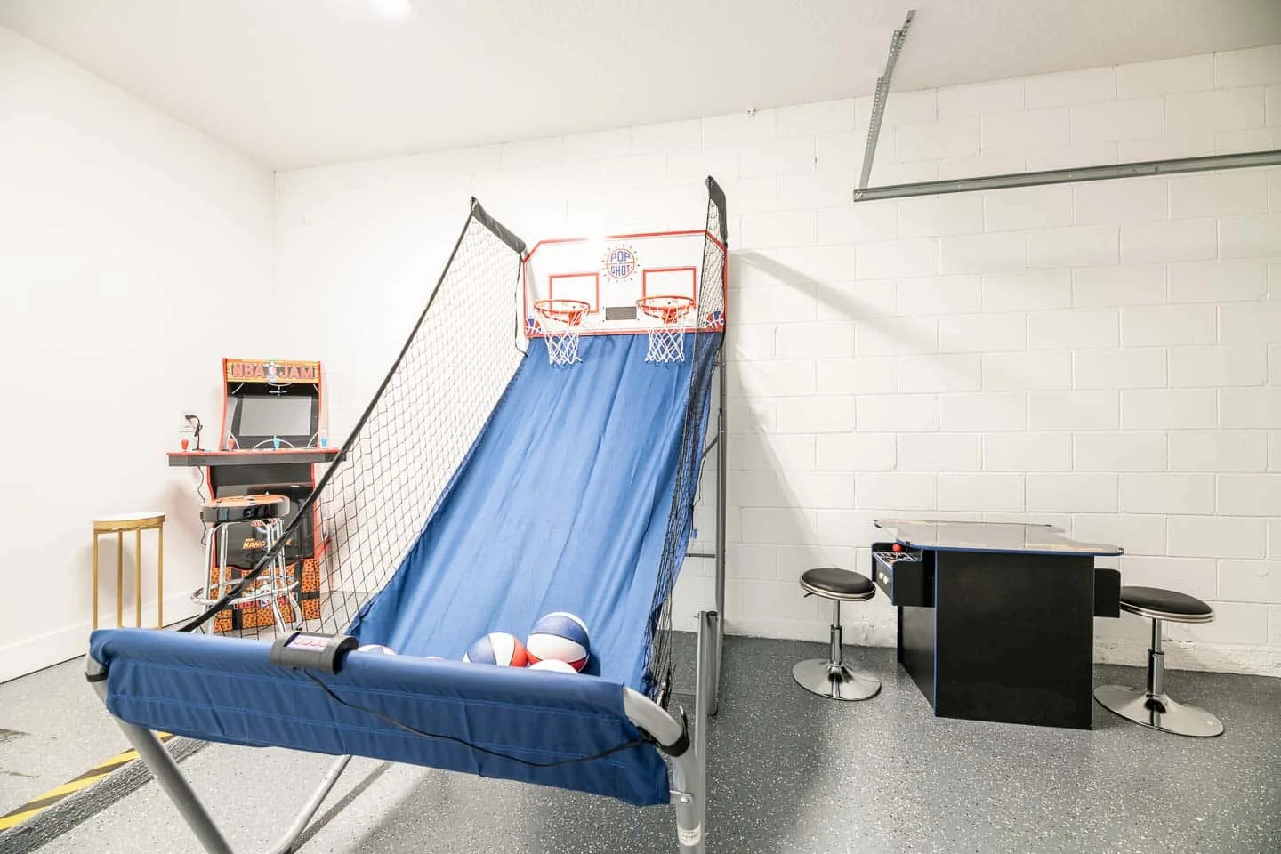 A recreation room features a basketball arcade game and a small counter with stools.
