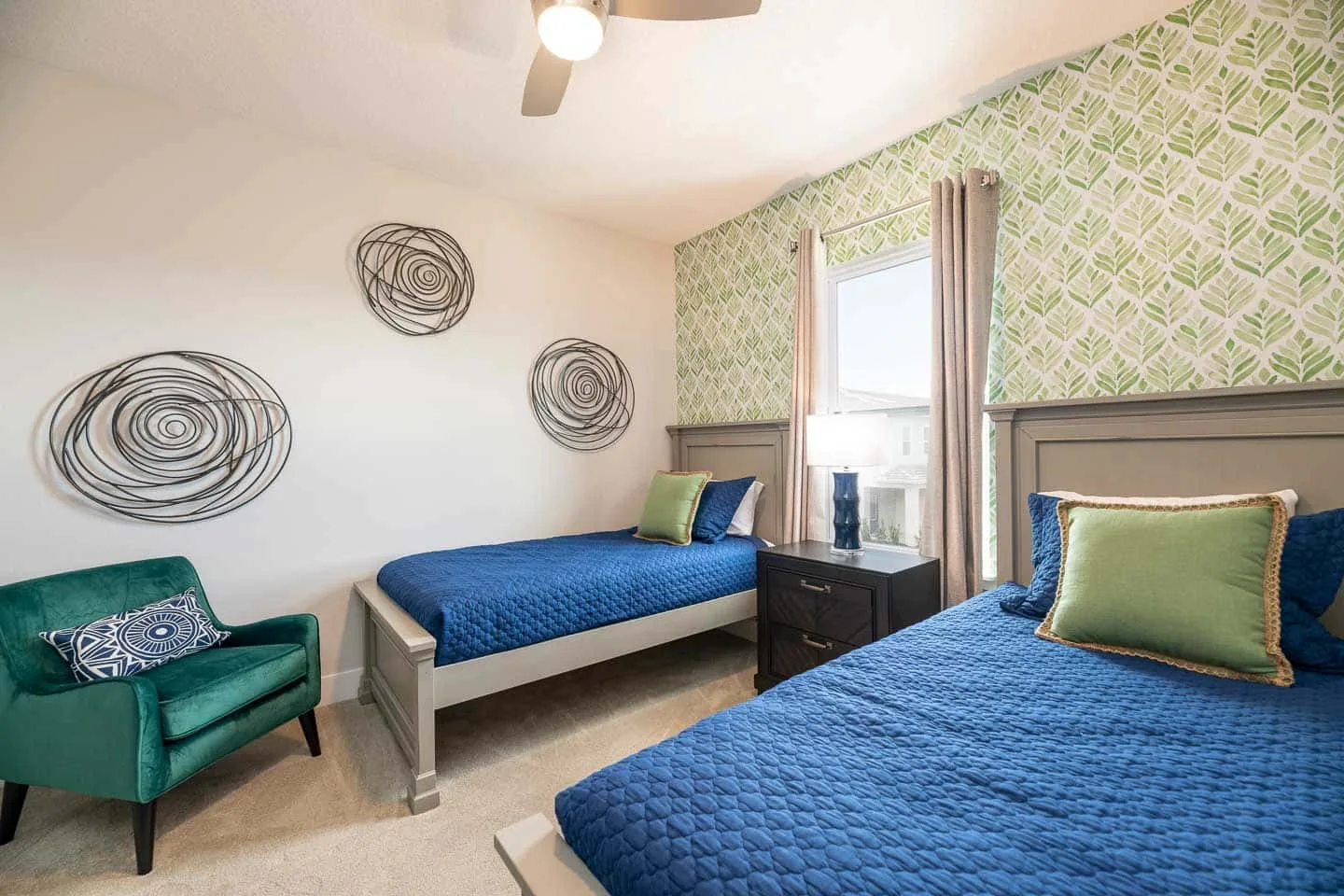A bedroom with two beds dressed in blue bedding and a green upholstered seat.
