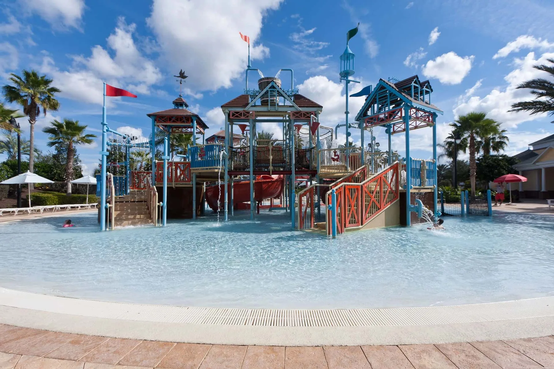 An outdoor water play area with colorful climbing structures and a shallow pool.