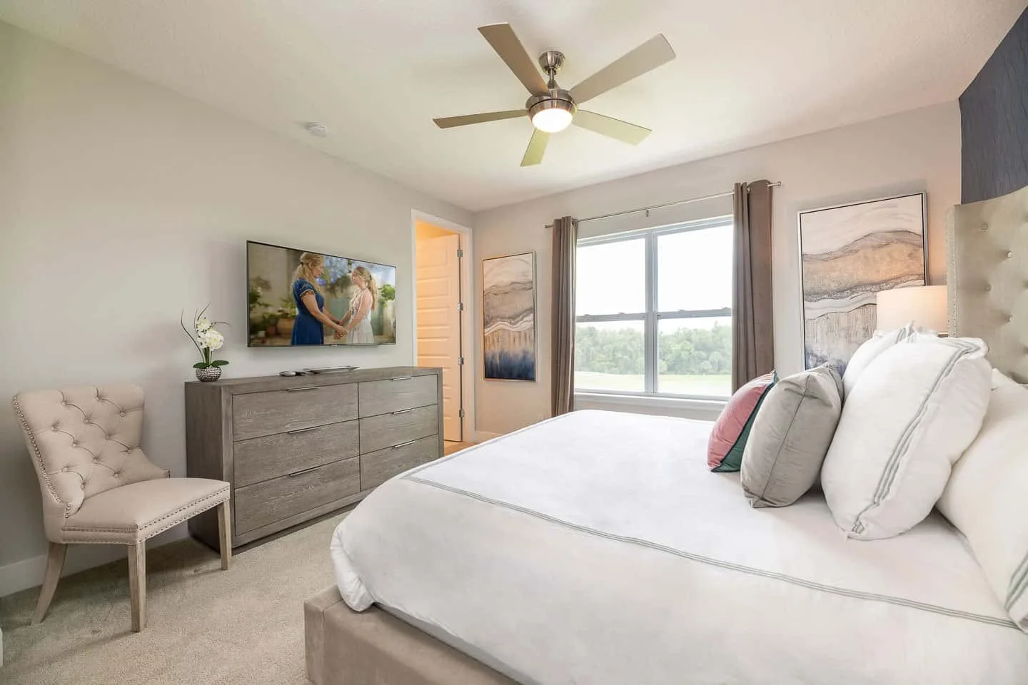A bright bedroom with a large bed, dresser, and window overlooking greenery.