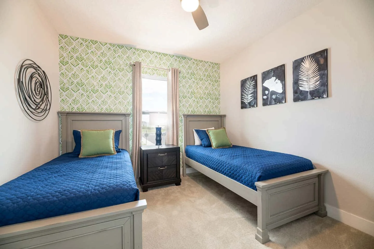 A bedroom with two single beds, blue bedding, and a window between them.