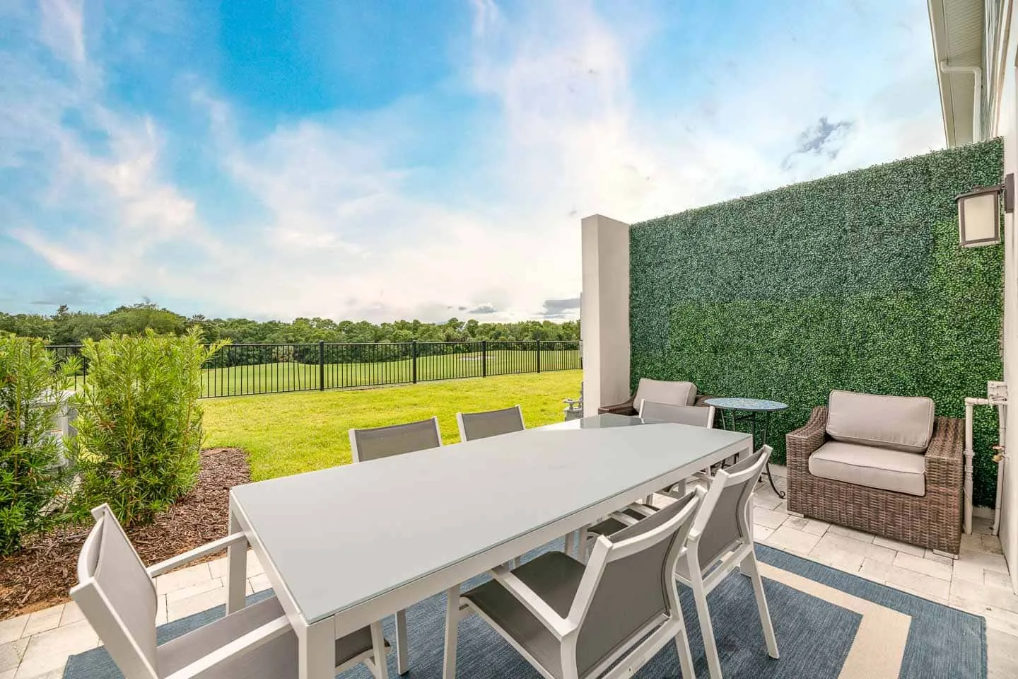 An outdoor dining patio with a long table and seating beside a green privacy screen.