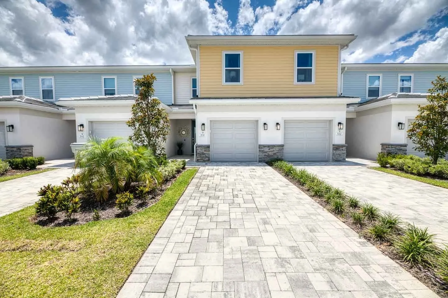 A row of attached homes with garages faces a paved driveway and landscaped lawn.