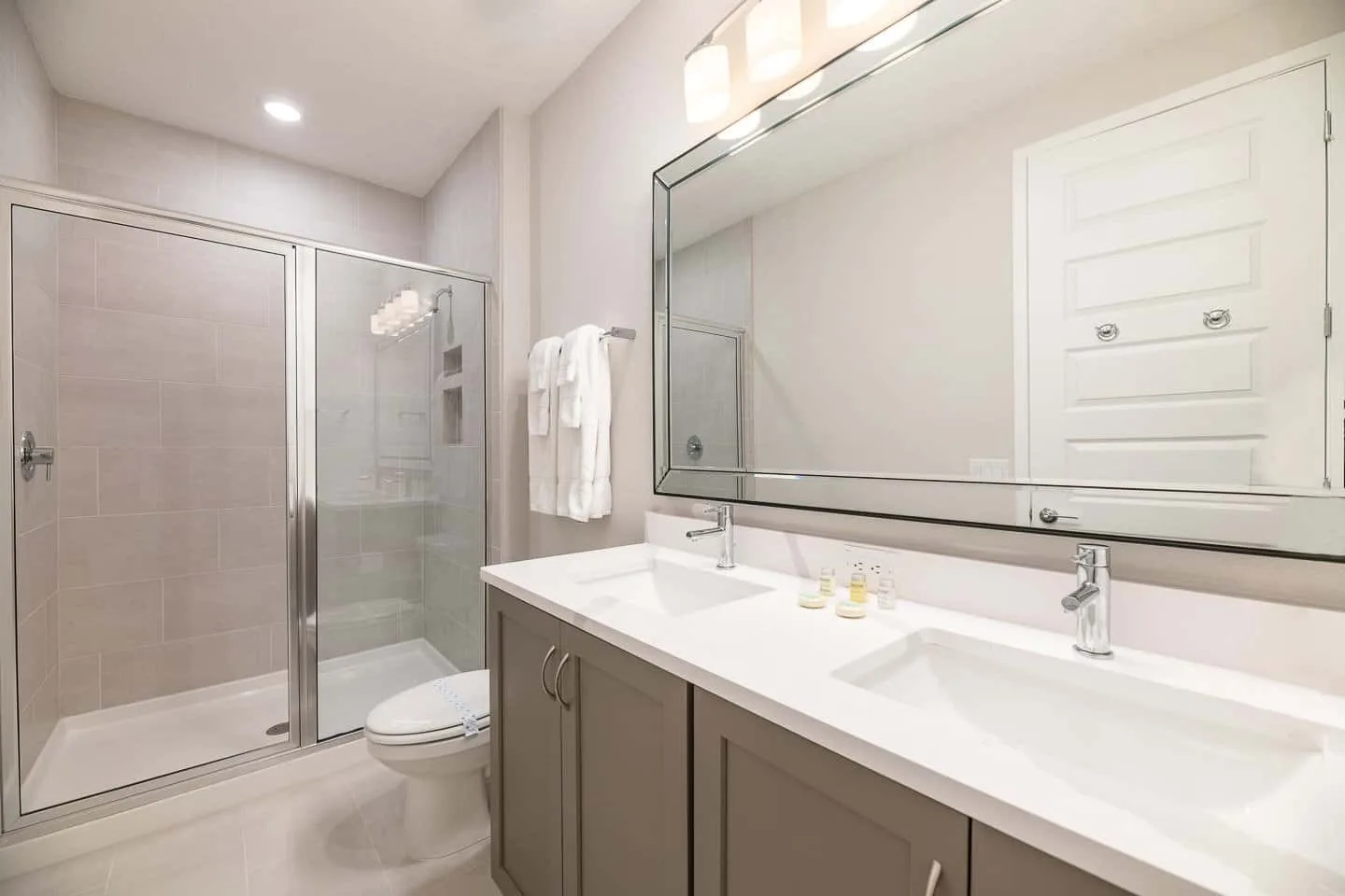 A bathroom with a glass shower, toilet, and double-sink vanity.