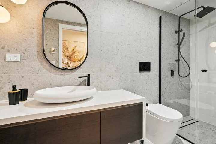 A modern bathroom with a vanity, mirror, toilet, and glass shower.