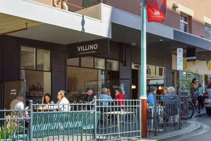 Street-level café seating extends along a storefront beneath a covered walkway.