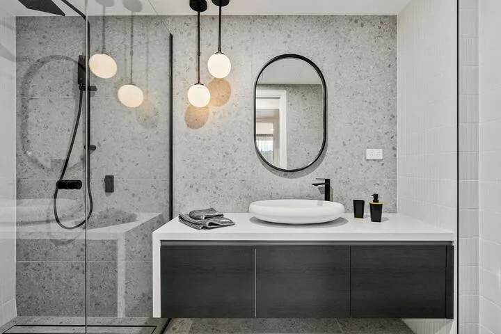 A modern bathroom with a glass shower, vanity, and oval mirror.
