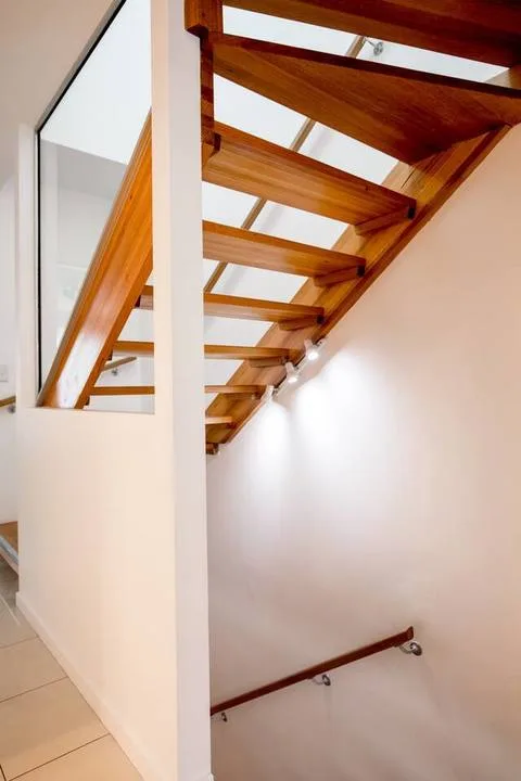 A staircase with wooden steps and a handrail runs along a white wall.