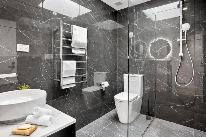 A modern bathroom with dark stone-patterned walls and a glass shower.