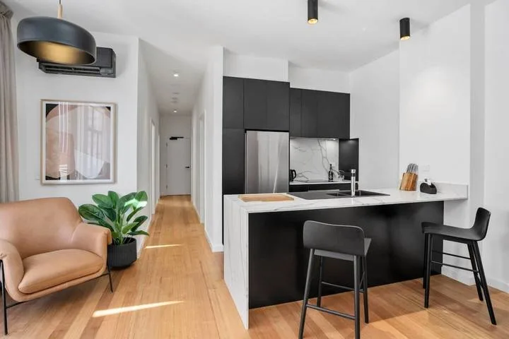 A modern kitchen and dining counter open onto a hallway, with seating nearby.