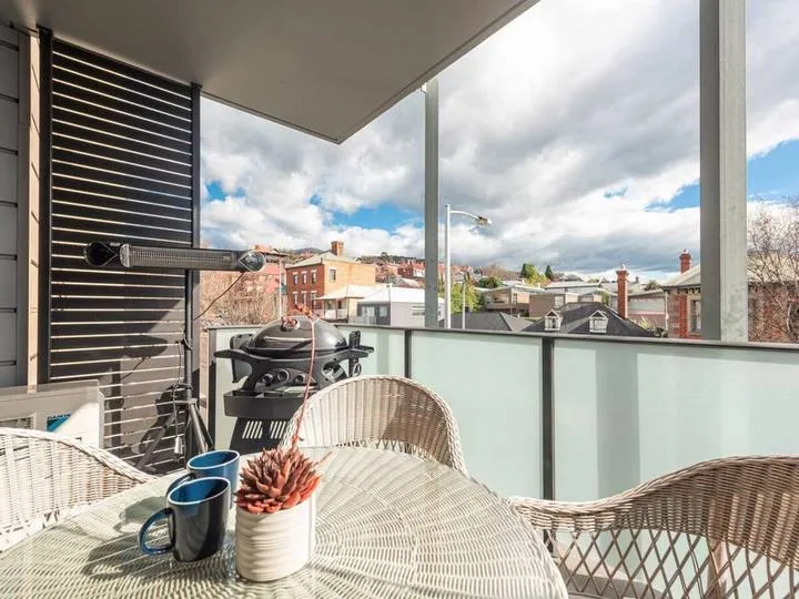 A balcony seating area with a barbecue grill and a view of nearby rooftops.