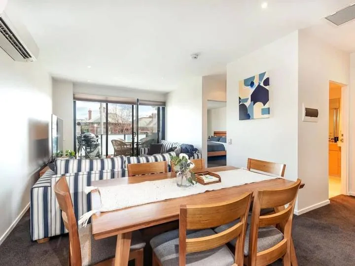 A dining area with a wooden table and seating beside large windows.