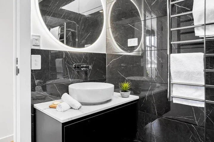A modern bathroom vanity with a round mirror and vessel sink.