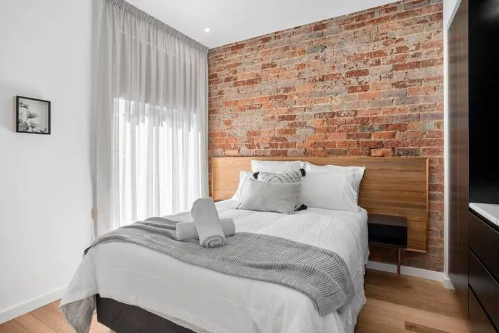 A bedroom with a bed, wood headboard, and exposed brick wall.