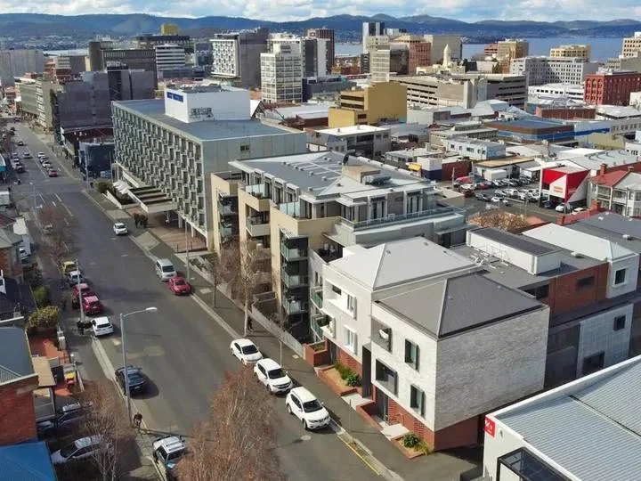 Aerial view of a city street lined with low-rise buildings and taller buildings beyond.