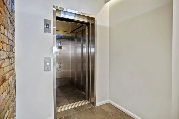 An open elevator sits beside an exposed brick wall in a bright hallway.