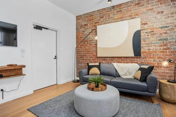 A living room with a gray seating area, round table, and exposed brick wall.