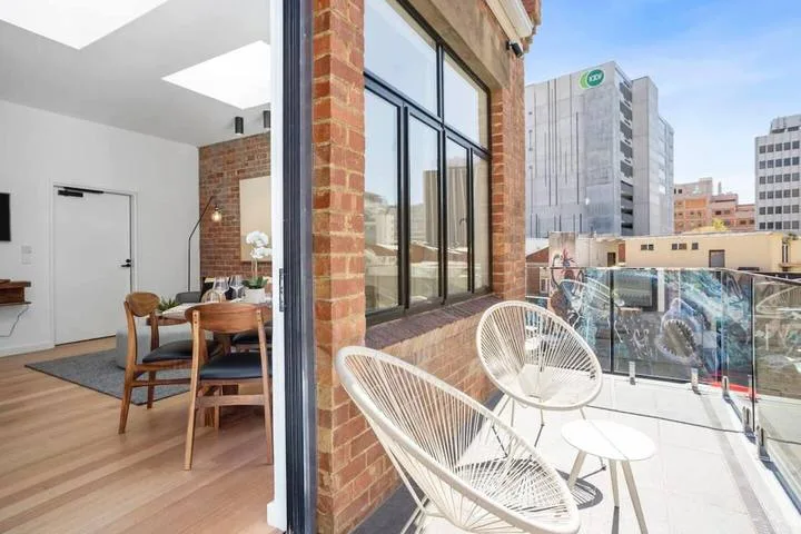 An open dining area beside a balcony with outdoor seating and nearby buildings.
