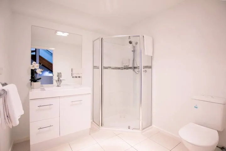 A bright bathroom with a vanity, glass shower, and toilet.