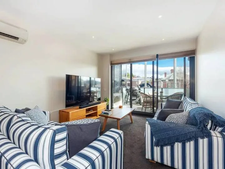 A living room with striped seating, a television, and glass doors opening onto a balcony.