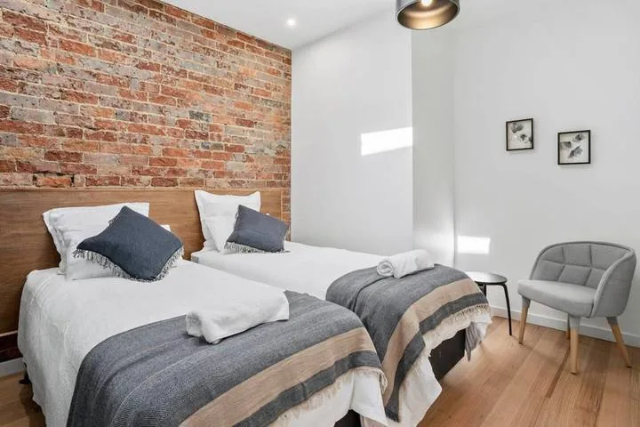 A bedroom with two beds, white bedding, and an exposed brick wall.