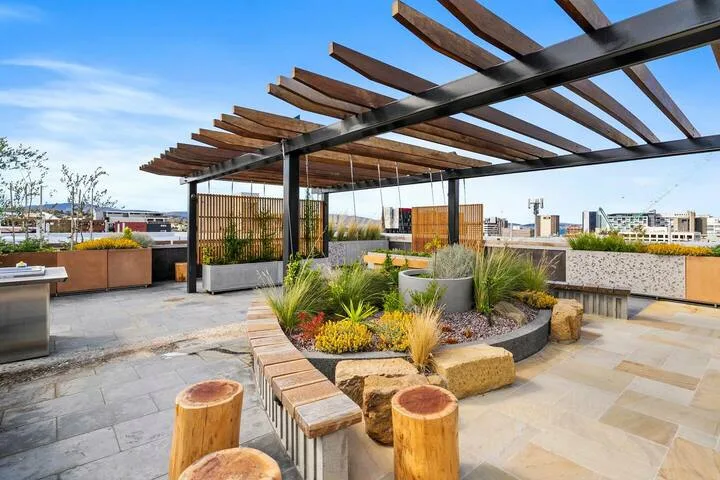 A rooftop terrace with a wooden pergola and landscaped seating area.