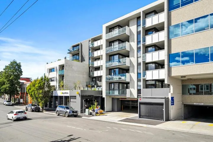 A modern multi-story building with balconies and storefronts along a city street.