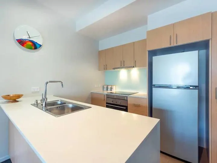 A modern kitchen with a large island, sink, and stainless steel refrigerator.