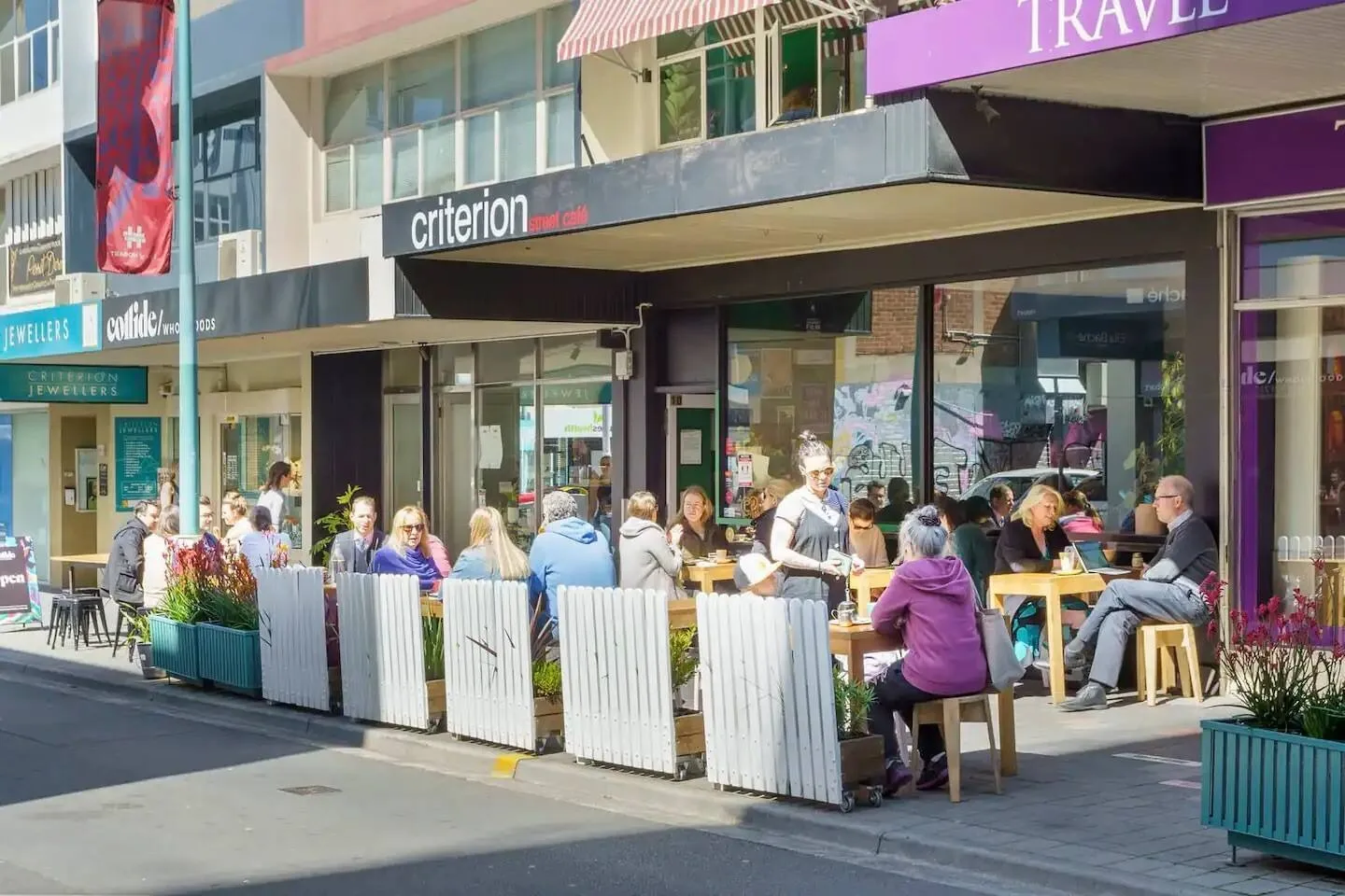 Mesas al aire libre ocupan la acera frente a varios comercios.