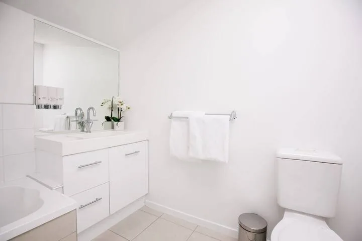 A bright bathroom with a sink, mirror, towel rail, and toilet.