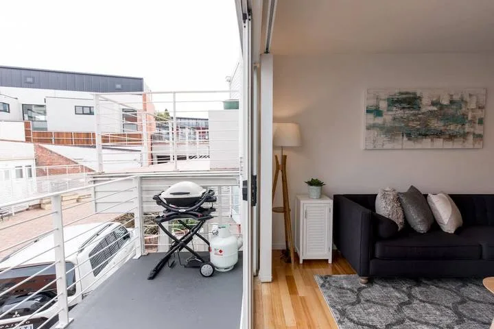A living room opens onto a balcony with seating and a grill.