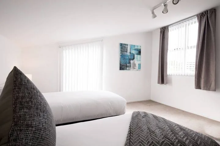 A bright bedroom with a white bed, large windows, and curtains.