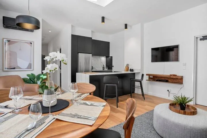 A modern dining and living area opens onto a compact kitchen with dark cabinetry.