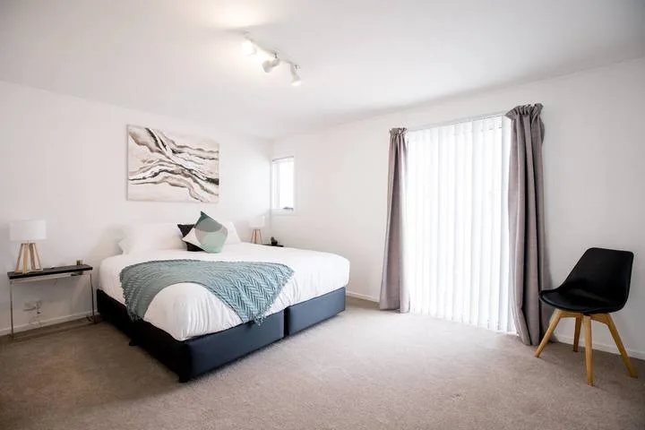 A bright bedroom with a neatly made bed and a curtained glass door.