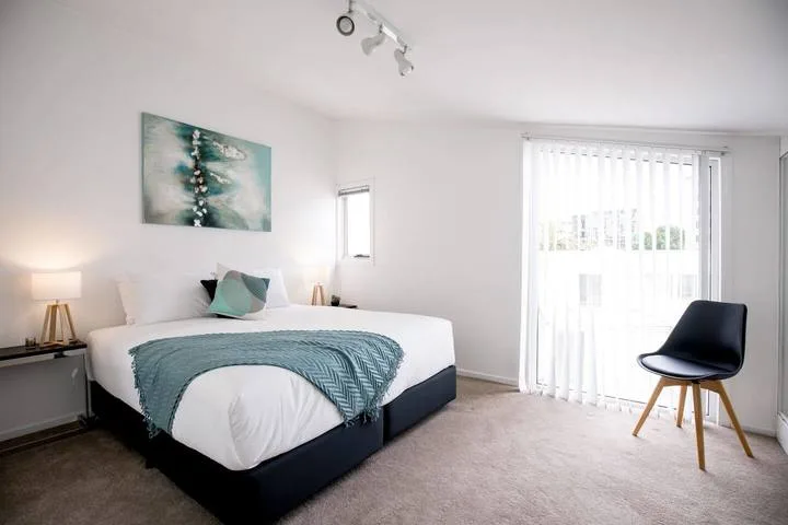 A bright bedroom with a bed, bedside lamps, and a large window.