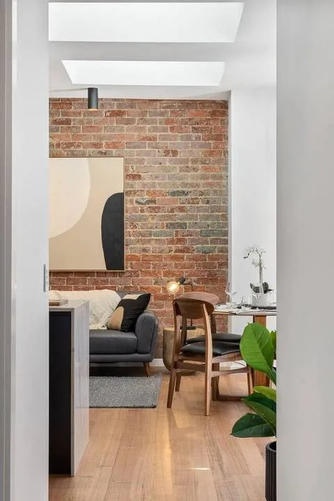 A living room with a brick wall, seating, and a wooden dining table.