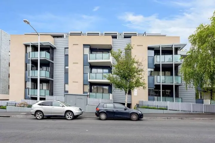 A modern apartment building stands beside a street with parked cars.