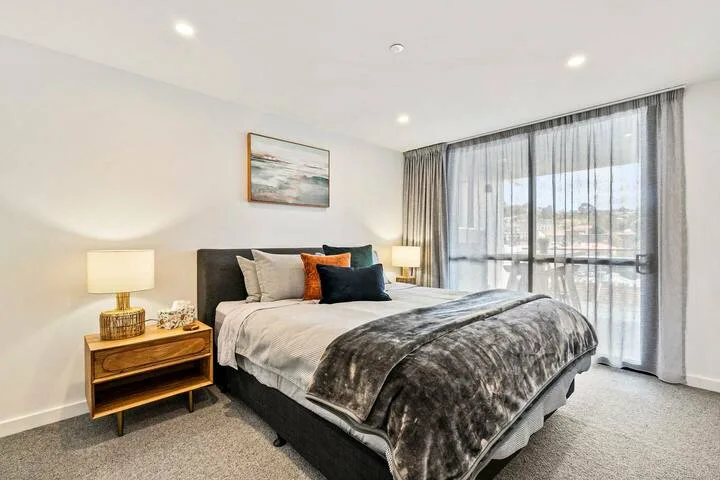 A bedroom with a neatly made bed beside large curtained windows.