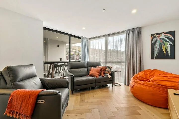 A living room with seating, a large orange beanbag, and windows covered by curtains.