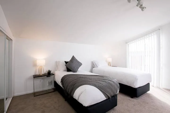 A bright bedroom with two beds dressed in white linens.