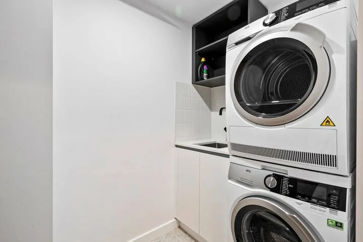 A laundry area with stacked washer and dryer beside a utility sink.