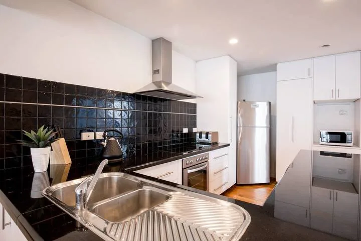 A modern kitchen with black tile backsplash, stainless steel appliances, and a double-basin sink.