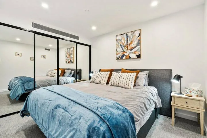 A bright bedroom with a bed, blue bedding, and mirrored closet doors.