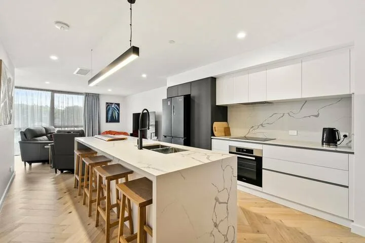 A modern kitchen with a large island and bar seating beside a living area.