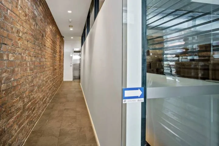 A narrow hallway runs between an exposed brick wall and glass partitions.